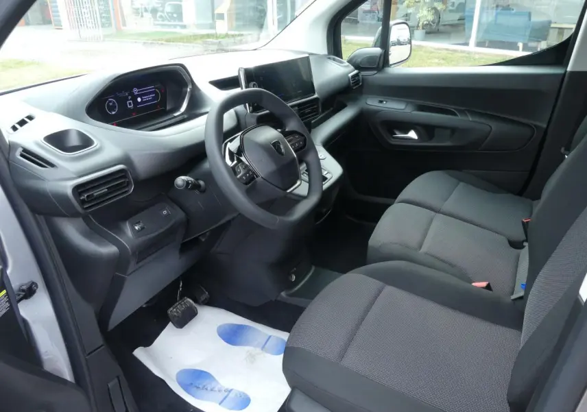 Vue intérieure côté conducteur du Peugeot Partner XL 2025, avec tableau de bord moderne et sièges tissu gris.