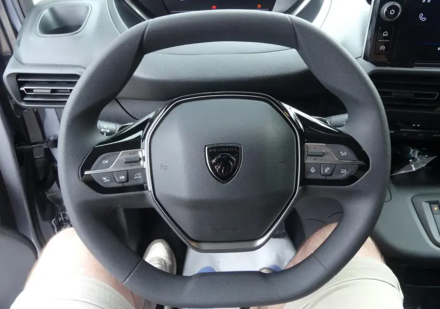 Vue rapprochée du volant multifonctions noir du Peugeot Partner XL 2025 avec tableau de bord et écran tactile visibles.