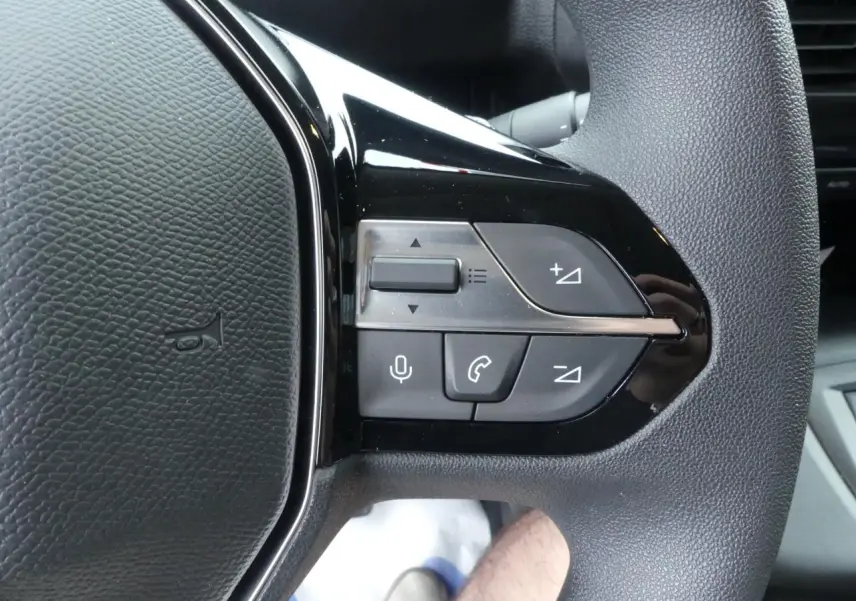 Gros plan sur les commandes du volant noir du Peugeot Partner XL 2025, boutons de volume et appel téléphonique visibles.