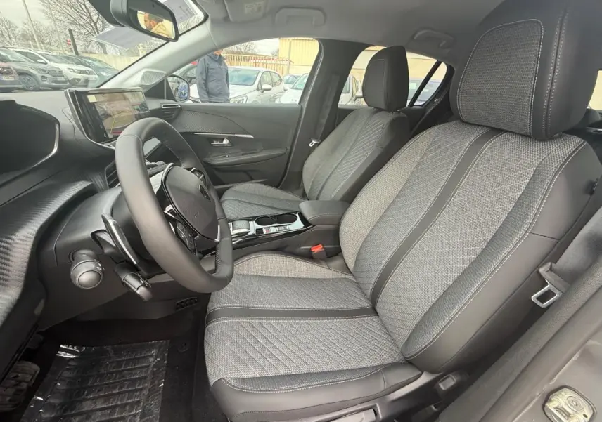 Vue intérieure côté conducteur de la Peugeot 208 Hybrid 145 Allure avec sièges gris à motifs et tableau de bord moderne.