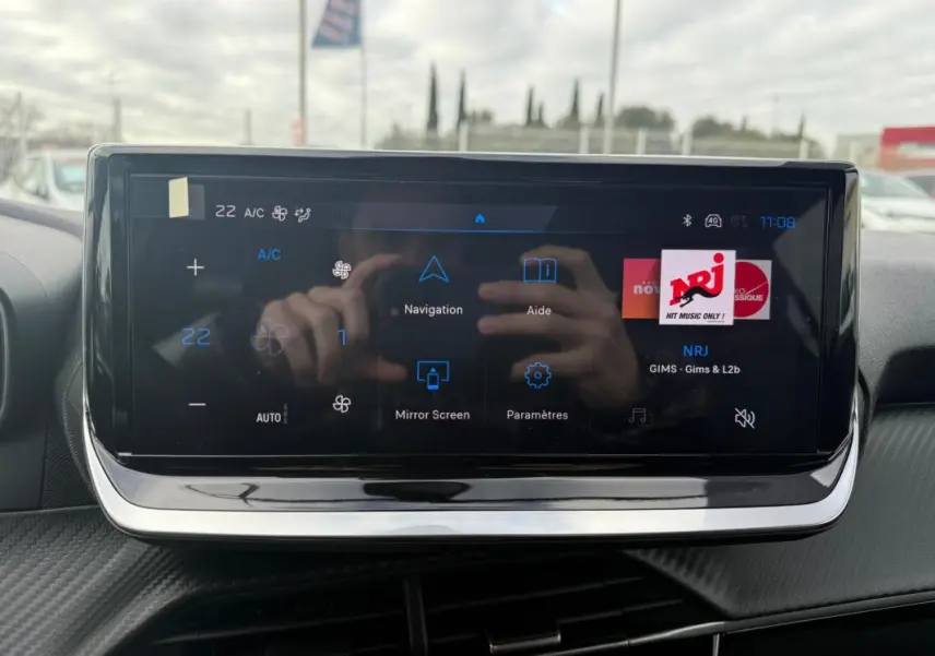 Écran tactile central du Peugeot 208 Hybrid 145 gris, affichant la radio NRJ et les options de navigation.