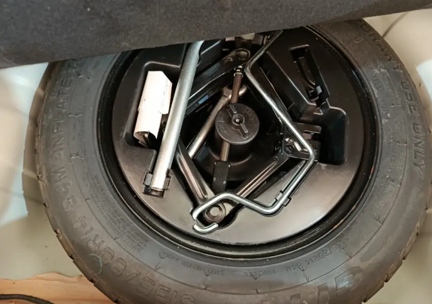 Gros plan sur la roue de secours et les outils de bord du coffre d'une Fiat 500 Hybrid blanche de 2022.