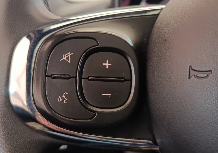 Gros plan sur les commandes du volant cuir noir de la Fiat 500 Hybrid Dolcevita 2022, boutons de volume et reconnaissance vocale.