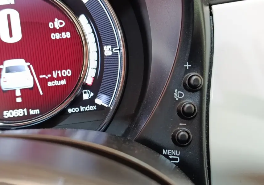 Gros plan sur le compteur digital rouge de la Fiat 500 blanche, avec boutons de réglage des phares à droite.