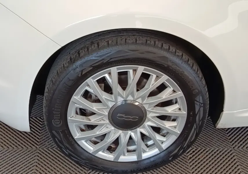 Gros plan sur la roue arrière droite d'une Fiat 500 blanche, avec jante argentée au design étoilé.