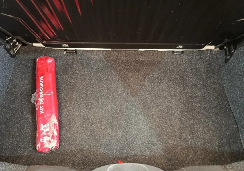 Coffre ouvert d'une Fiat 500 blanche, vue de dessus, avec un kit de sécurité rouge posé à gauche.