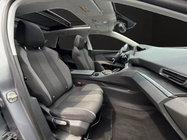 Vue intérieure côté gauche de la Peugeot 208 gris platinium, montrant sièges tissu, volant cuir multifonctions et tableau de bord tactile.