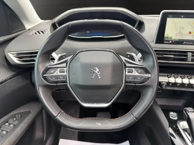 Vue rapprochée du volant cuir noir multifonctions de la Peugeot 208 gris platinium, avec tableau de bord et écran tactile visibles.
