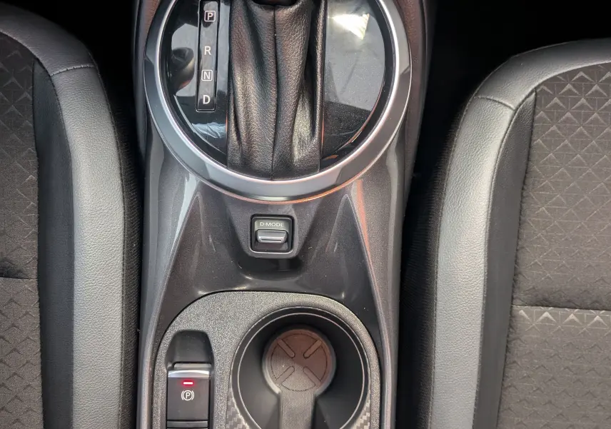 Vue plongeante sur la console centrale noire du Nissan Juke gris, avec levier de vitesses automatique et porte-gobelets.