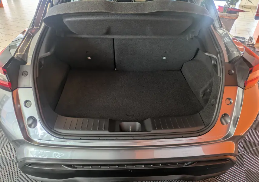 Coffre ouvert vu de l'arrière d'un Nissan Juke 2024 gris squale métal, montrant un espace de chargement propre et spacieux.