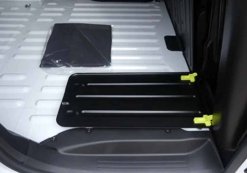 Vue rapprochée de la zone de chargement blanche du Peugeot Partner XL avec trappe noire et fixations jaunes visibles.