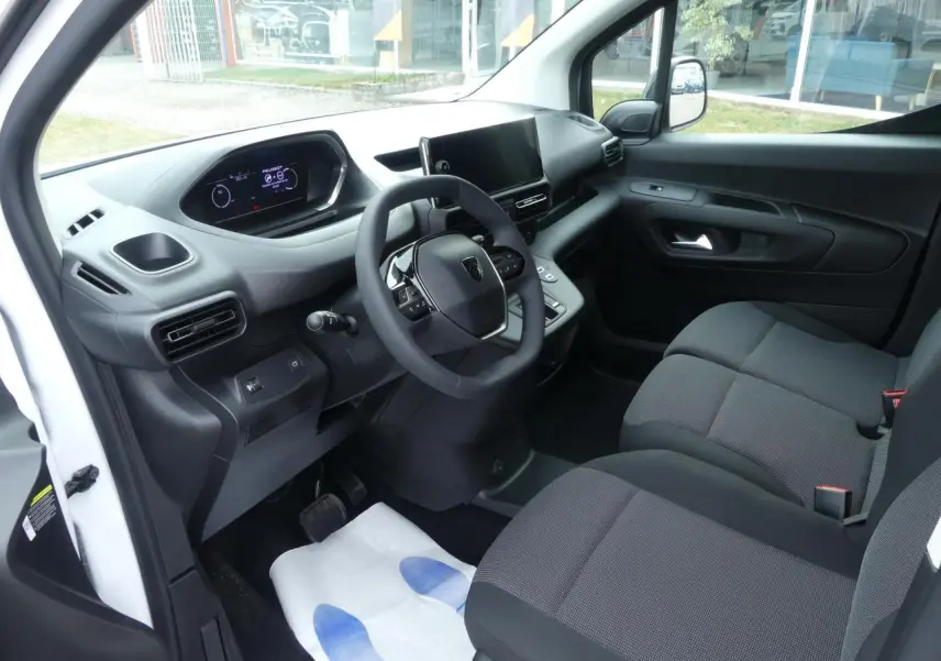 Intérieur du Peugeot Partner XL 2025 vu côté conducteur, tableau de bord moderne avec écran tactile et sièges tissu gris.