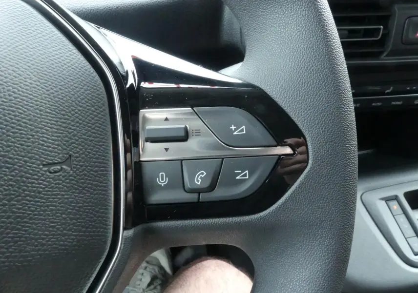 Gros plan sur les commandes multifonctions du volant côté gauche du Peugeot Partner blanc 2025.