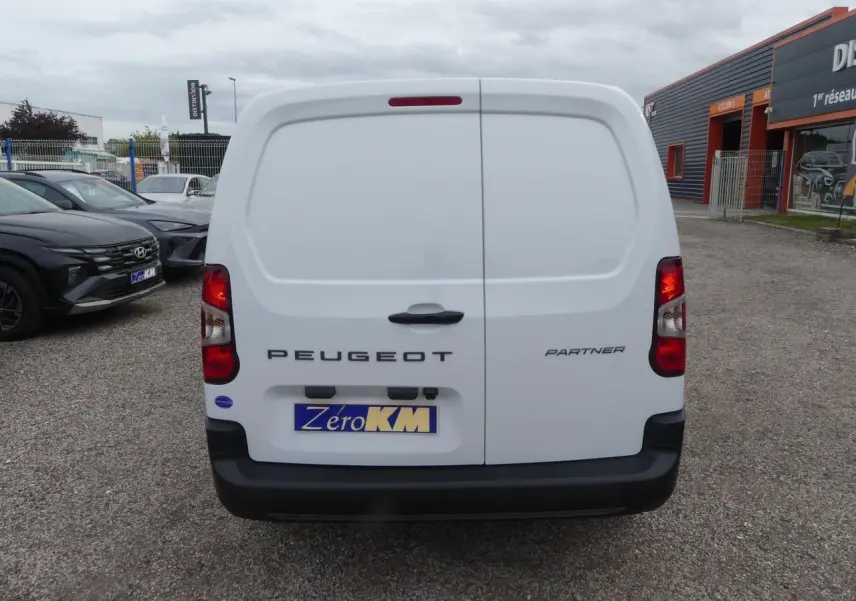 Vue arrière d'un Peugeot Partner blanc avec portes battantes et pare-chocs noir sur un parking.