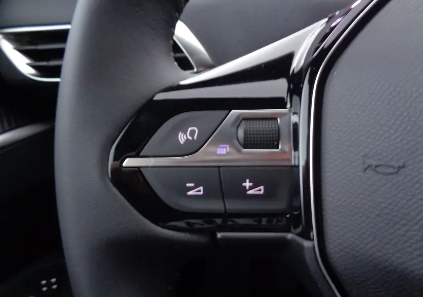 Gros plan sur les commandes gauche du volant en cuir noir du Peugeot 3008 gris Artense 2023, boutons de volume et appel.
