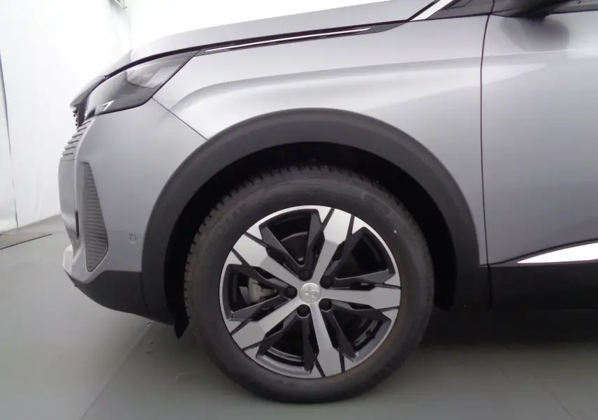Gros plan sur la roue avant gauche et l'aile d'un Peugeot 3008 gris Artense métallisé, mettant en valeur la jante bicolore moderne.
