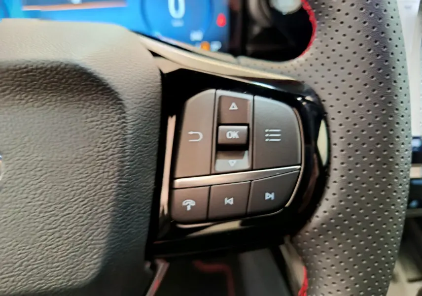Gros plan sur les commandes multifonctions à droite du volant en cuir perforé avec surpiqûres rouges du Ford Puma 2025.