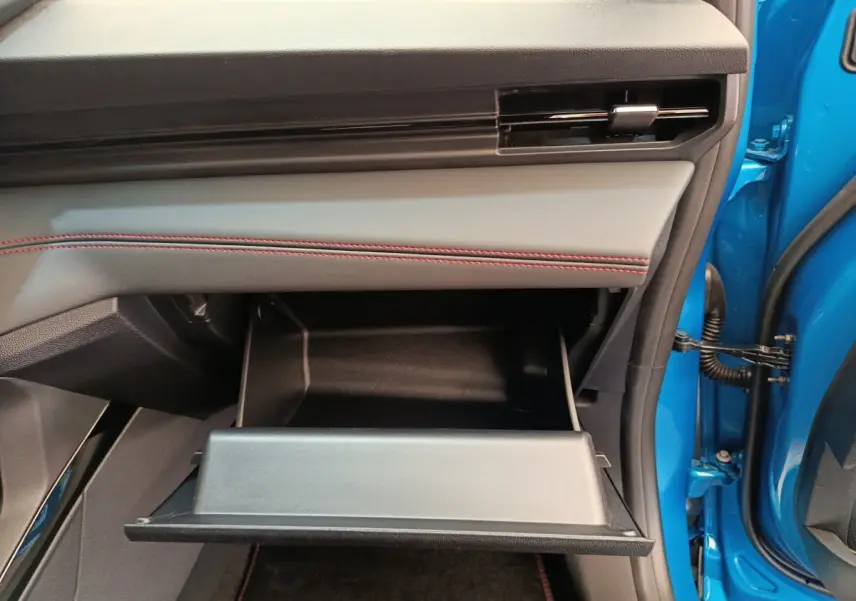 Gros plan sur la boîte à gants ouverte côté passager du Ford Puma bleu avec surpiqûres rouges sur le tableau de bord.