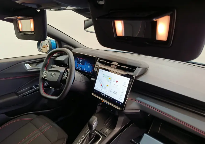 Vue intérieure côté conducteur du Ford Puma bleu 2025, tableau de bord avec écran tactile et volant cuir noir à surpiqûres rouges.