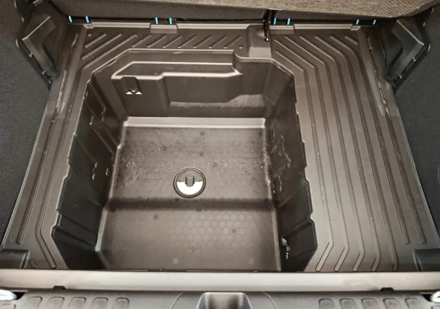 Vue plongeante sur le coffre modulable du Ford Puma 2025, montrant le compartiment de rangement sous tablette en plastique noir.