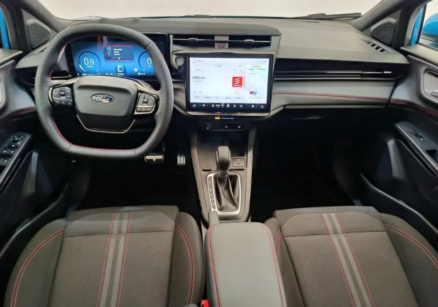 Intérieur du Ford Puma 2025 en vue frontale, tableau de bord noir avec écran tactile central et volant cuir noir à surpiqûres rouges