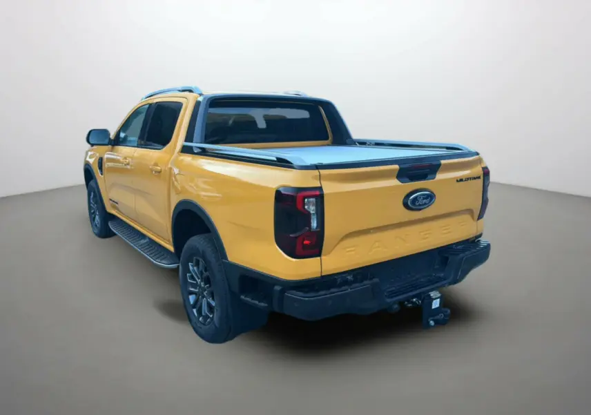 Ford Ranger 2025 Cyber orange en 3/4 arrière droit, avec benne couverte et logo Wildtrak visible sur la porte.