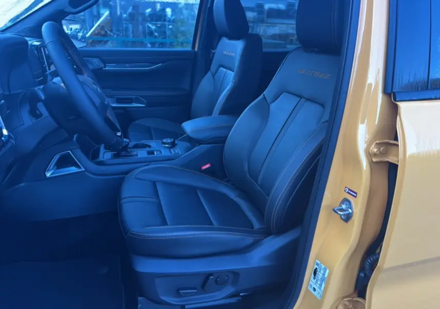 Intérieur du Ford Ranger 2025 Cyber orange, vue côté conducteur ouverte, sièges en cuir noir Wildtrak avec surpiqûres orange.