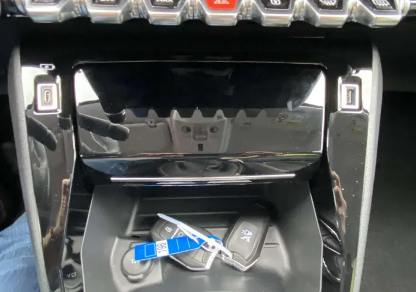 Gros plan sur la console centrale noire brillante du Peugeot 208 bleu, avec deux clés mains libres posées.