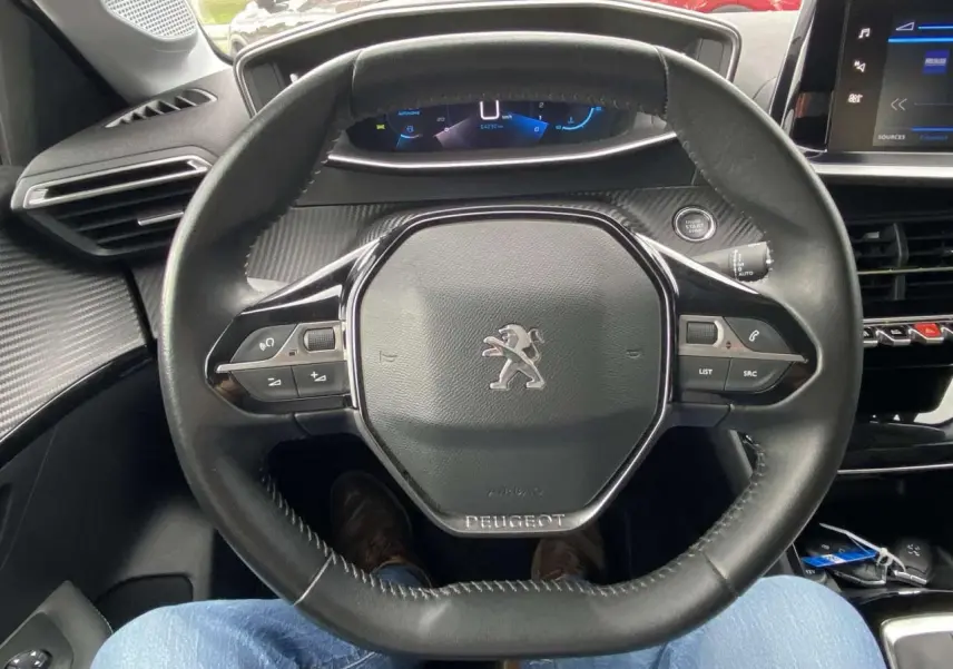 Vue rapprochée du volant cuir noir de la Peugeot 208 2020 avec commandes intégrées et tableau de bord digital.