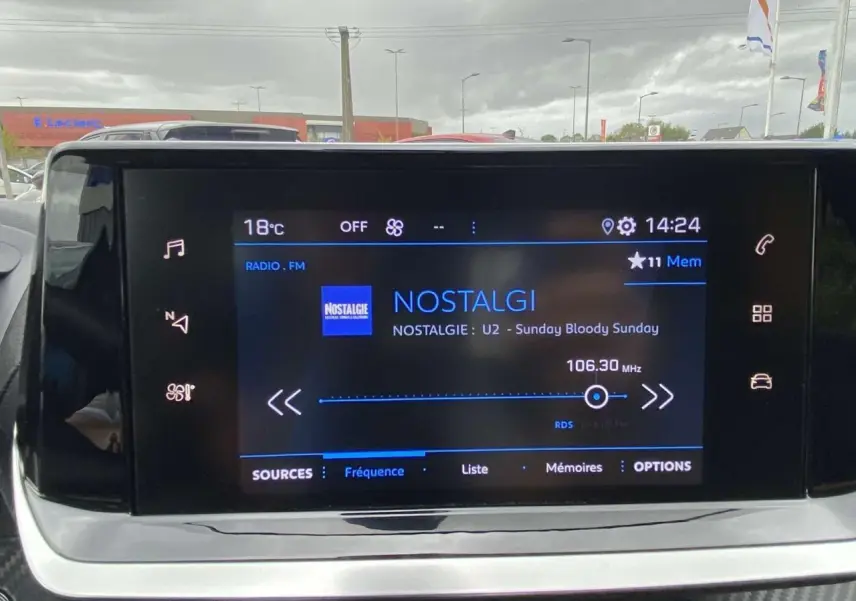 Écran tactile central de la Peugeot 208 bleu, affichant la radio sur la fréquence 106.30 MHz en intérieur véhicule.