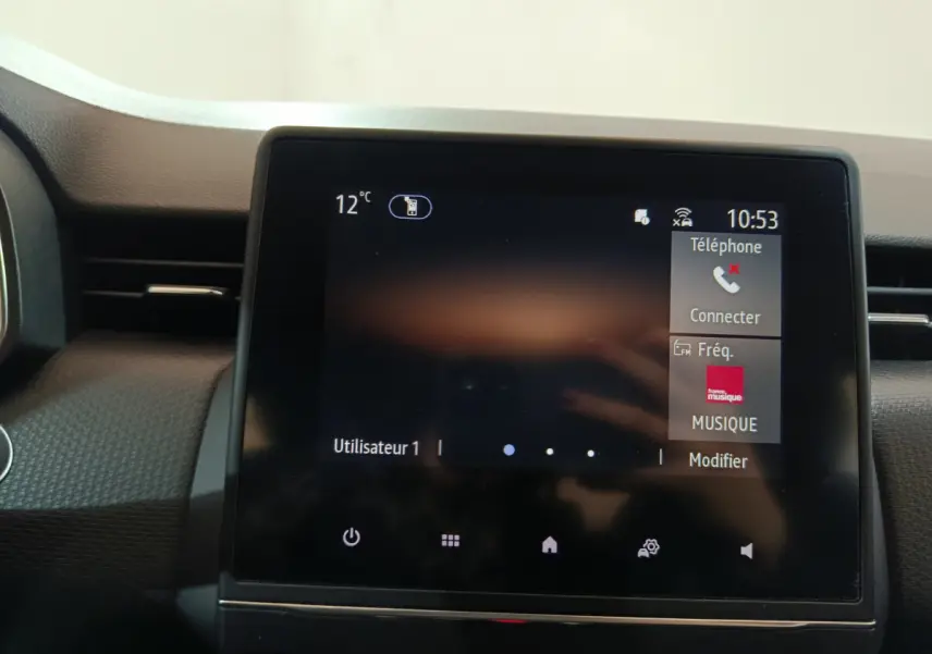 Écran tactile central affichant la température et options multimédia dans l'habitacle d'une Renault Clio blanche.