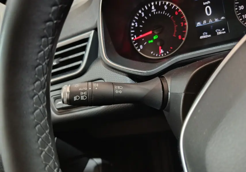 Gros plan sur la manette de phares et clignotants à gauche du volant cuir d'une Renault Clio Business blanche, tableau de bord allumé.