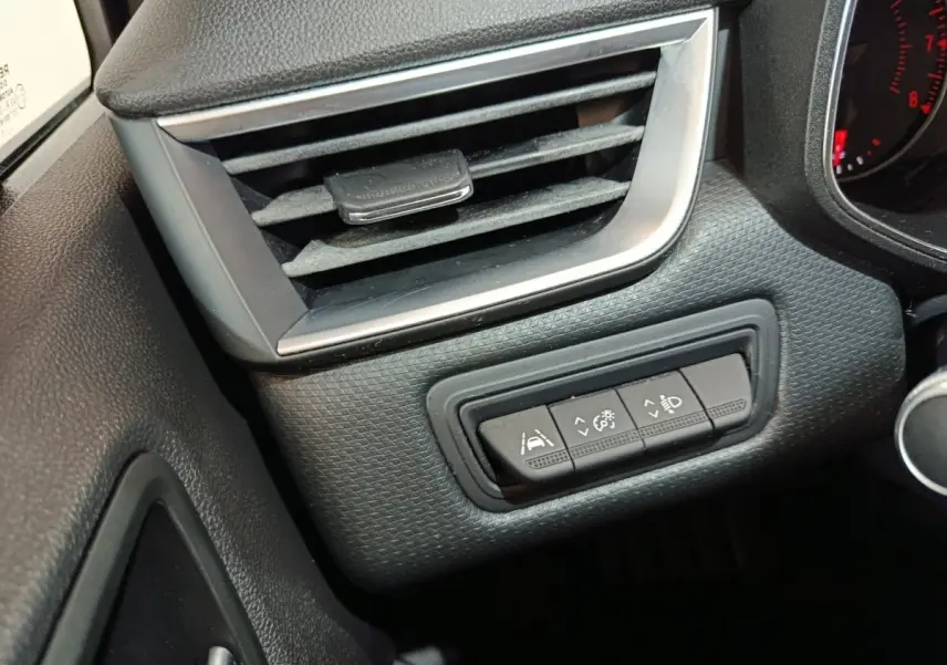 Gros plan sur la console gauche du tableau de bord noir de la Renault Clio Business TCe 90 avec commandes d'assistance et ventilation.