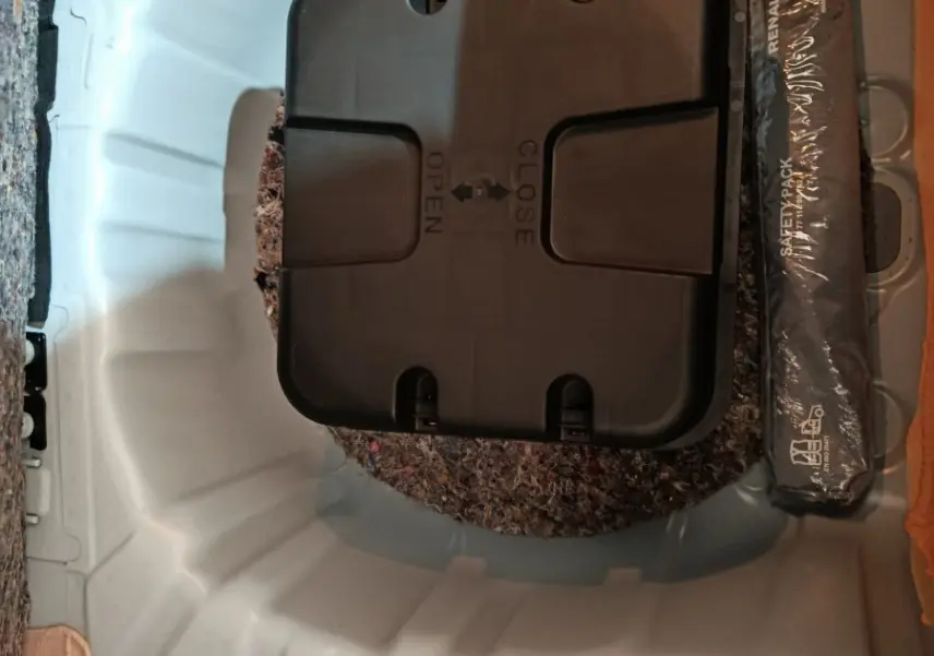 Vue plongeante sur le coffre blanc de la Renault Clio Business TCe 90, montrant le compartiment de rangement avec kit de sécurité.