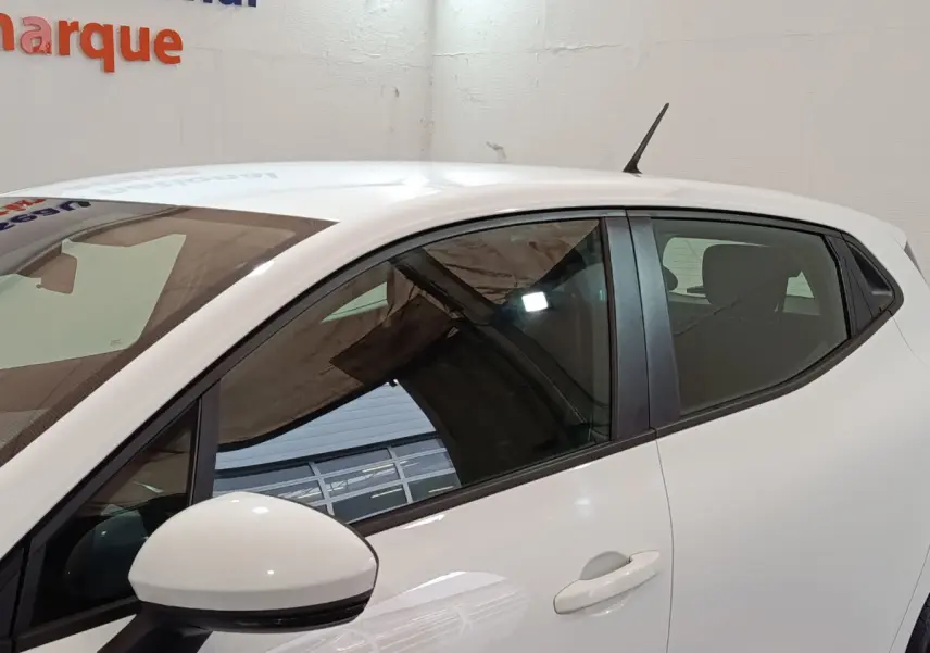 Profil côté gauche d'une Renault Clio Business TCe 90 blanche, avec rétroviseur et antenne visibles sur fond intérieur.