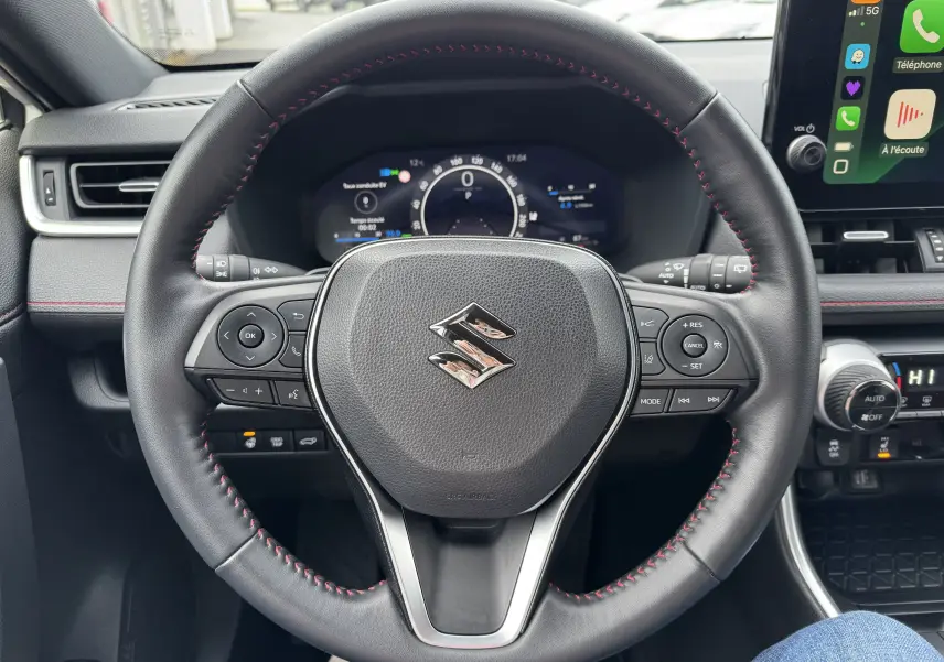 Vue rapprochée du volant en cuir noir avec surpiqûres rouges du Suzuki Across hybride rechargeable 2023, tableau de bord numérique visible.