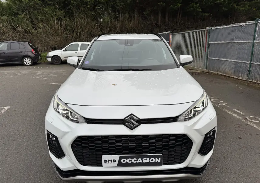Vue frontale d'un Suzuki Across blanc 2023 avec calandre noire et phares LED, stationné en extérieur sur parking.