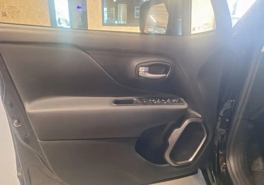 Vue intérieure de la porte côté gauche noire du Jeep Renegade 2024 avec haut-parleur et commandes électriques visibles.