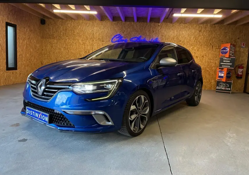 Renault Mégane 1.7 BlueDCI 150 GT Line bleu vue 3/4 avant droit en intérieur avec jantes alliage et phares allumés.