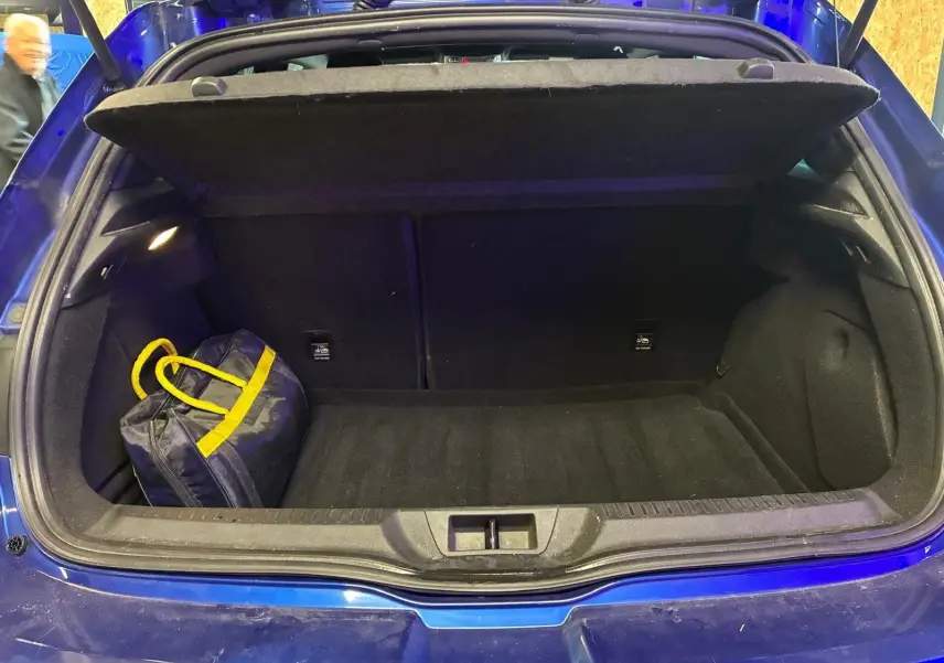 Coffre ouvert d’une Renault Mégane bleu 2019, vue arrière, avec un sac noir à anses jaunes à l’intérieur.