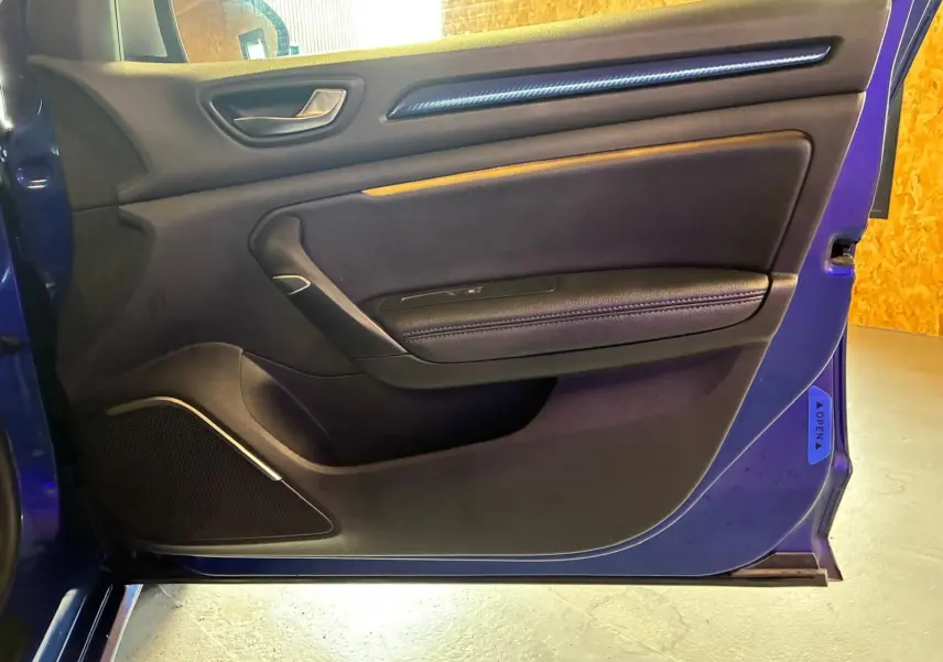 Vue de profil intérieur de la porte avant gauche d'une Renault Mégane bleu 2019 avec garniture noire et poignée argentée.