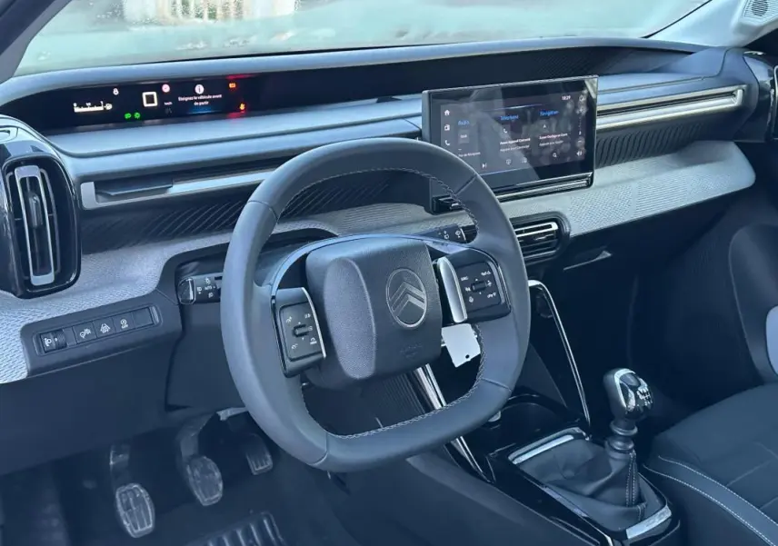 Vue intérieure côté conducteur de la Citroën C3 2025 noire, volant multifonction, écran tactile et levier de vitesses manuel.