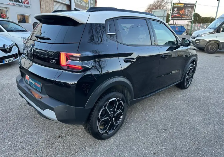 Vue 3/4 arrière droite d'une Citroën C3 noire 2025 avec jantes alliage 17 pouces et barres de toit visibles.