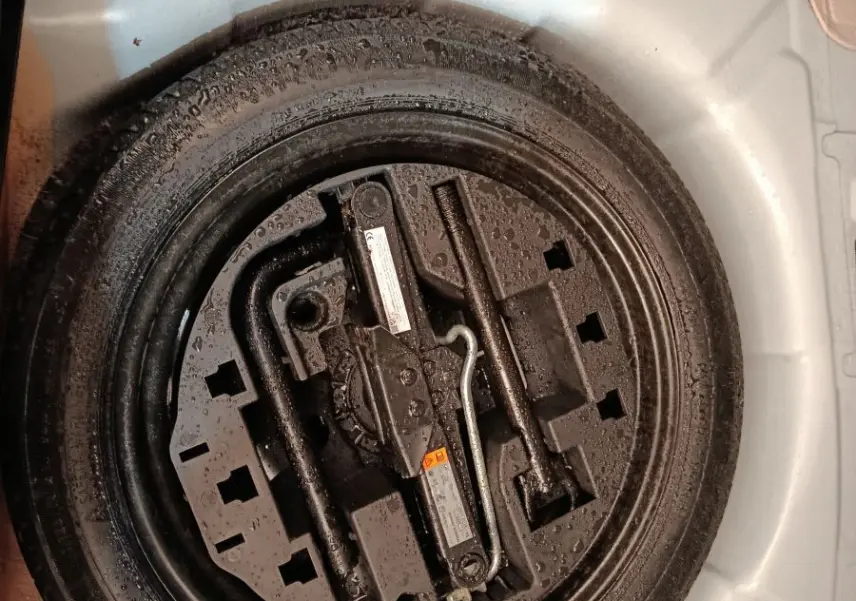 Vue plongeante sur la roue de secours noire et ses outils dans le coffre blanc d'une Renault Clio Business 2022.