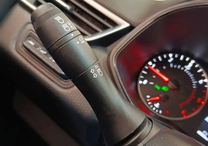Gros plan sur la manette de commande des phares et clignotants dans l’habitacle d’une Renault Clio blanche, tableau de bord en arrière-plan.