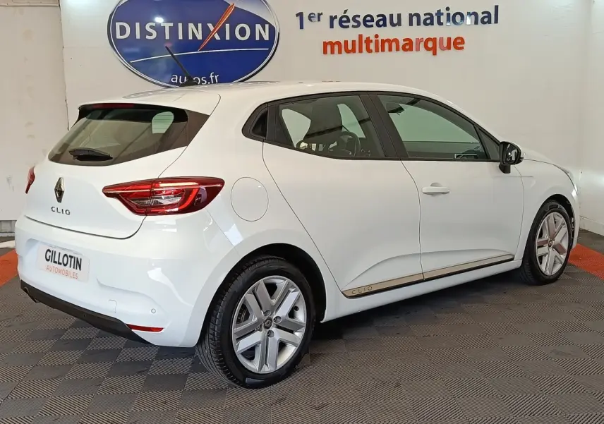 Vue 3/4 arrière droite d'une Renault Clio Business Blue dCi 100 blanche, avec jantes alliage et logo distinctif sur la porte.