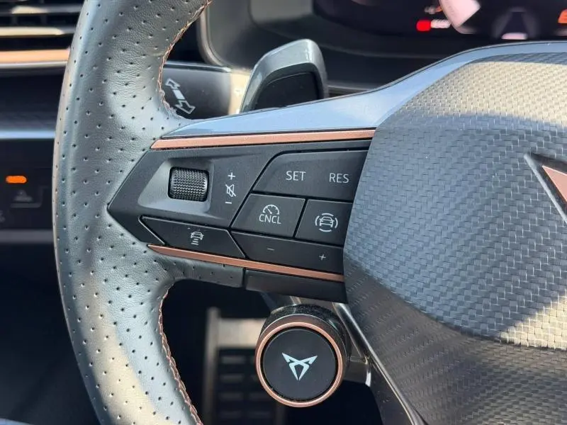 Gros plan sur la partie gauche du volant perforé noir du CUPRA Formentor 2025 avec commandes de régulateur et logo cuivre.