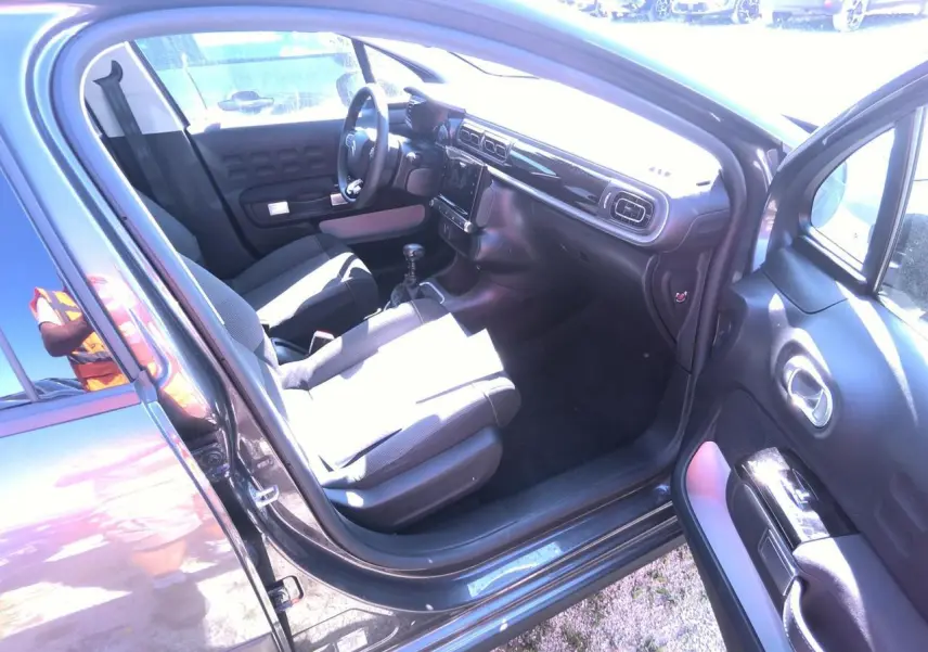 Intérieur côté conducteur de Citroën C3 gris foncé 2024, montrant sièges tissu gris et tableau de bord noir brillant.