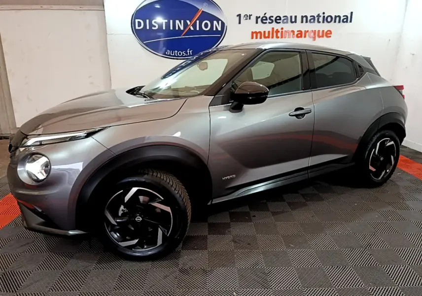 Nissan Juke Hybrid gris foncé vue de profil côté gauche dans un showroom avec jantes noires distinctives.