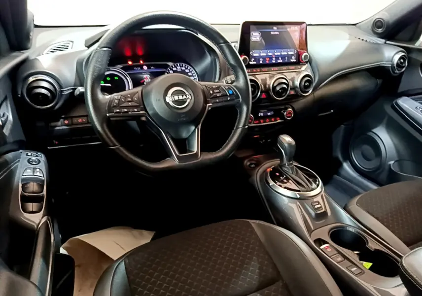 Vue intérieure côté conducteur du Nissan Juke Hybrid 143 Business+ 2023 avec volant cuir, écran tactile et levier de vitesse automatique.